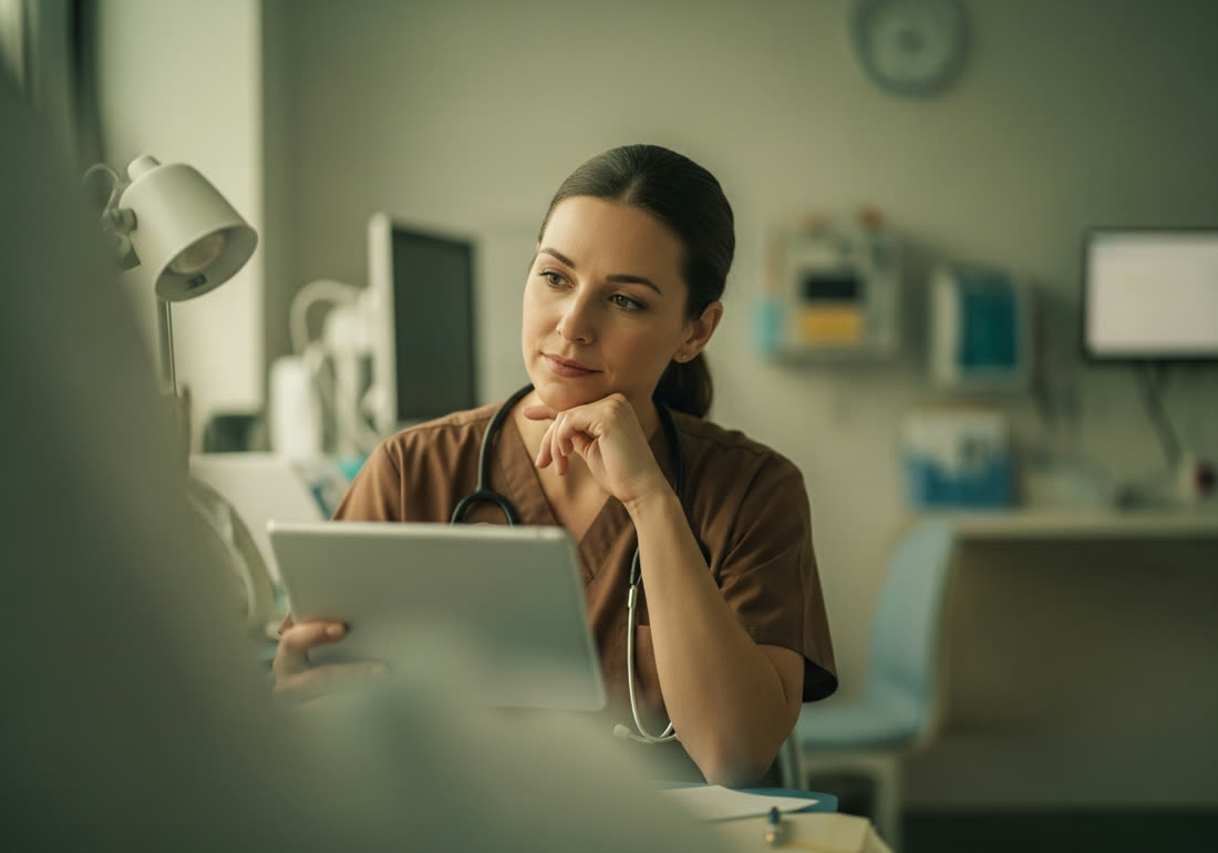 A nurse reviewing a tablet at a bright hospital nurses' station